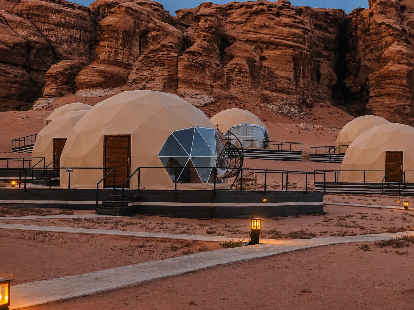 A desert landscape with multiple dome-shaped tents, each with a door and a small porch area.