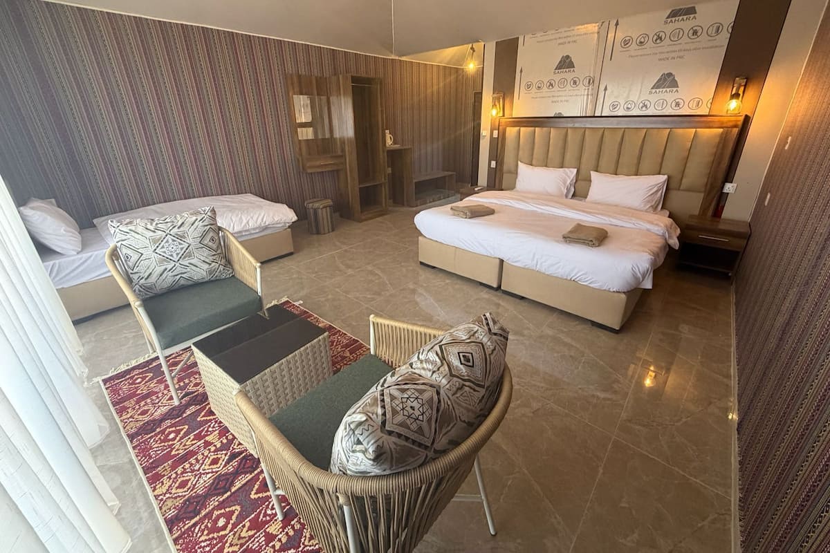 A hotel room with a large bed, two sofas, a small table, and a patterned rug.