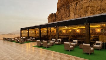 An outdoor seating area with wicker chairs and a green carpet, overlooking a desert landscape.