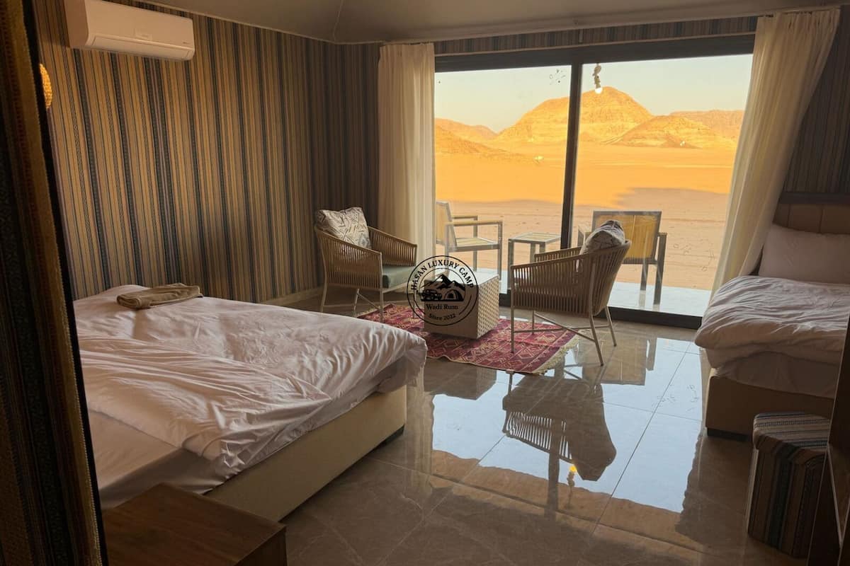 A hotel room with two beds, a large window with a desert view, a small table, and a chair.