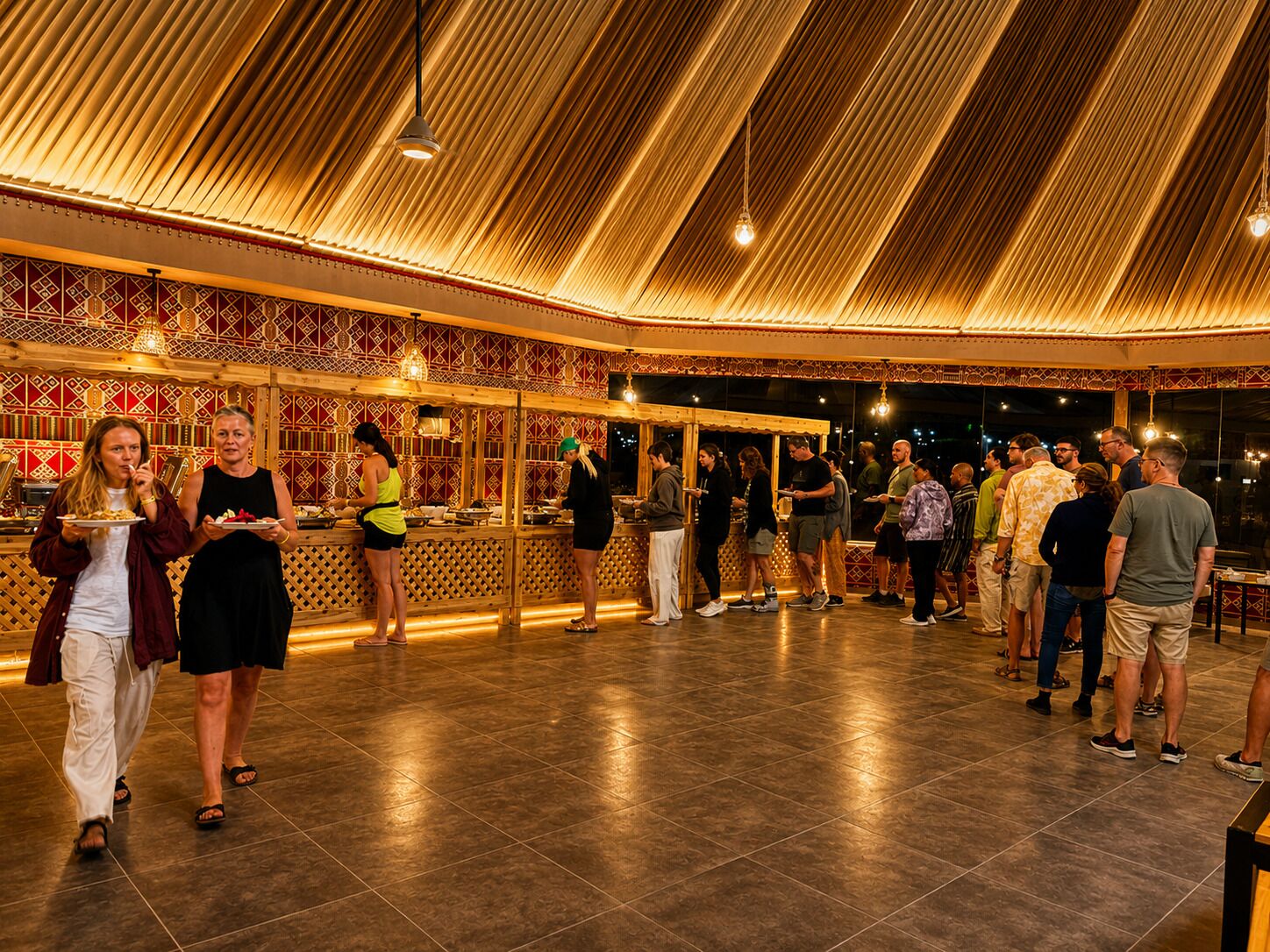 An indoor venue with a high ceiling and patterned walls, featuring a group of people dining and conversing.