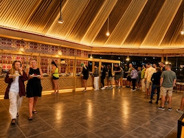Un espacio interior con techo alto y paredes con diseño, donde un grupo de personas cena y conversa.