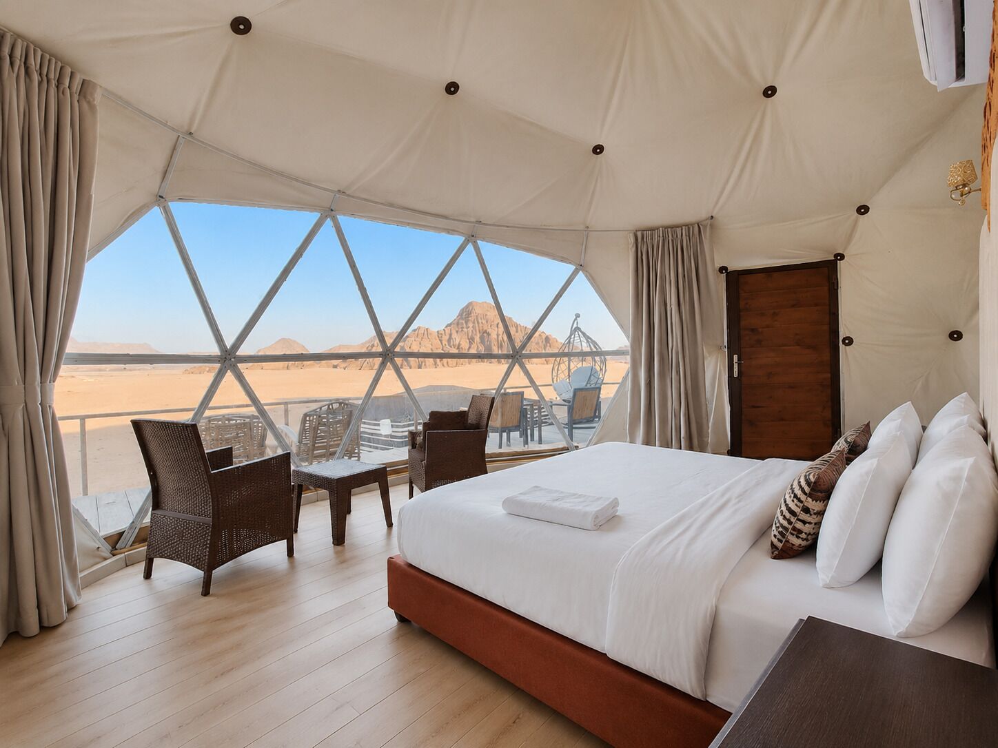 A tented room with a bed, chairs, and a view of a desert landscape.