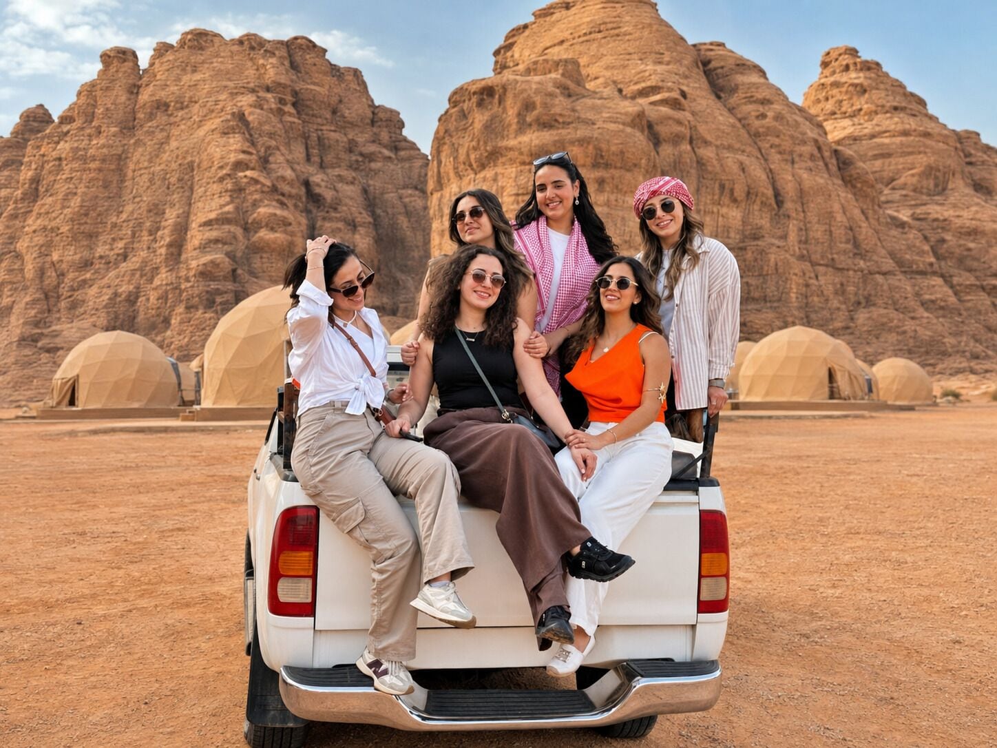 A group of people seated on the back of a vehicle with a desert landscape and rock formations in the background.