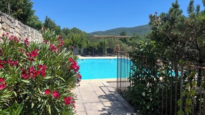 A swimming pool with a pergola and lounge chairs, surrounded by greenery and a stone wall. -  Bastide 1830, Domaine de la Bastidonne 4* Superb view of le Luberon Heated Pool (Céreste)
