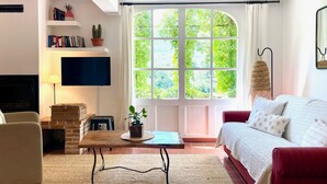 A living room with a sofa, a coffee table, a TV, and a large window with a view of greenery. - Lavender, Luberon view, swimming pool, AC : Villa Mas du Luberon 15 km from Apt (Céreste)