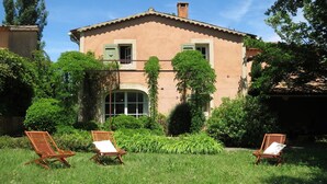 A two-story building with a garden in front, featuring two wooden lounge chairs and a large arched window. - Lavender, Luberon view, swimming pool, AC : Villa Mas du Luberon 15 km from Apt (Céreste)