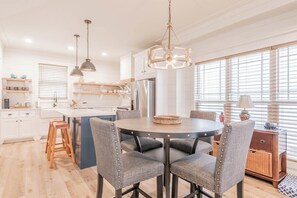 A modern kitchen with a central island, pendant lighting, and a dining area with a round table and chairs.