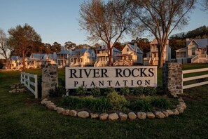 A sign for River Rocks Plantation with a stone border and a white picket fence.