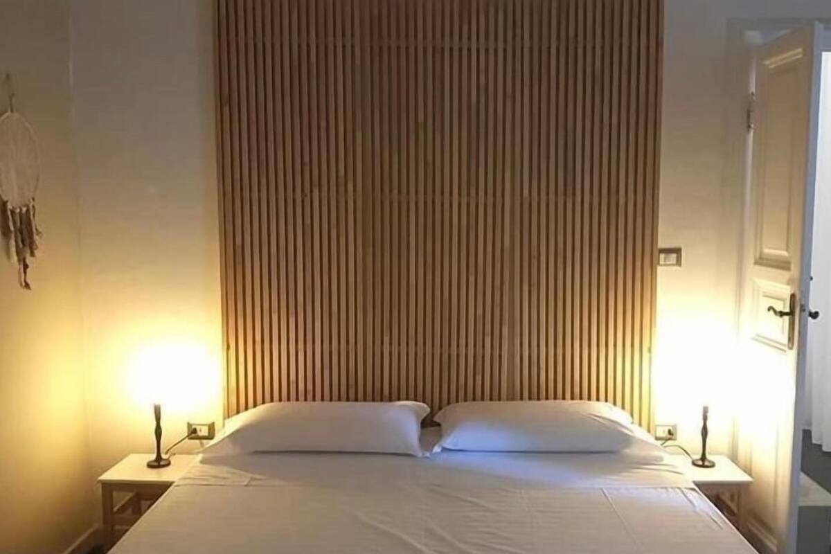 A neatly made bed with white linens, flanked by two bedside tables with lamps, in a room with vertical wooden paneling on the wall.
