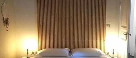 A neatly made bed with white linens, flanked by two bedside tables with lamps, in a room with vertical wooden paneling on the wall.