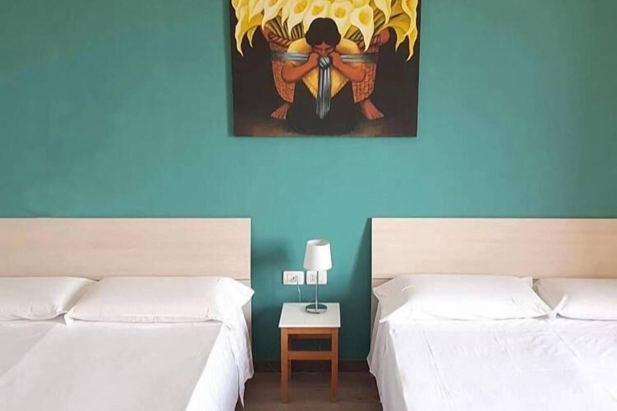 A hotel room with two beds, a small bedside table with a lamp, and a painting on the wall.
