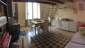 Una sala de estar con sofá, una mesa de comedor con sillas, una zona de cocina con armarios y una escalera.
