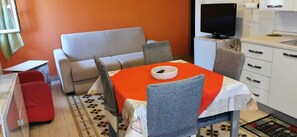 Un coin repas avec une table dressée pour deux personnes, un canapé et un téléviseur en arrière-plan.