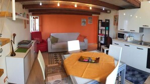 Un espacio habitable compacto con kitchenette, un sofá, una mesa de comedor y una estantería.