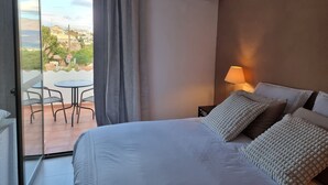 Habitación de hotel con cama, mesita de noche, lámpara, ventana con cortinas y vistas al exterior.