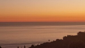 Un paisaje costero con un atardecer sobre el agua, edificios en la orilla y un cielo despejado.
