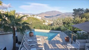 Área de piscina en la azotea con sillones y vistas a montañas.