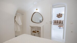 Et soveværelse med seng, stol, et spejl på væggen og en dør til en balkon med sofa og puder.