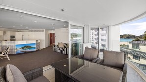 A modern living area with a balcony, a kitchen, and a dining area. - A strand Of Paradise, Oceanside & Views with pool (Mount Maunganui)
