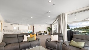 A spacious living area with two leather sofas, a glass coffee table, and a view of a cityscape through large windows. - A strand Of Paradise, Oceanside & Views with pool (Mount Maunganui)