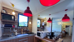 Una cocina moderna con microondas integrado, estufa a gas y armarios de madera. Hay luces colgantes rojas tipo farol y una ventana con vistas a zonas verdes.