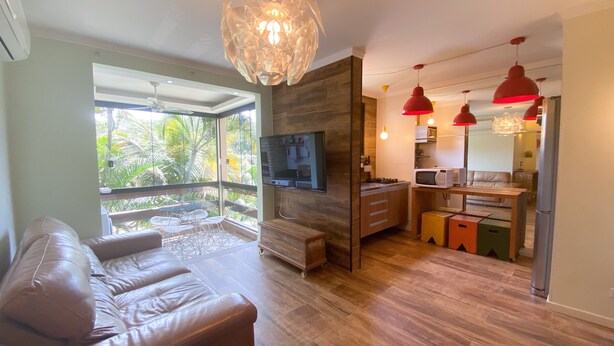 Una sala de estar moderna con un sofá de cuero, una zona de comedor de madera y una cocina con lámparas colgantes rojas.