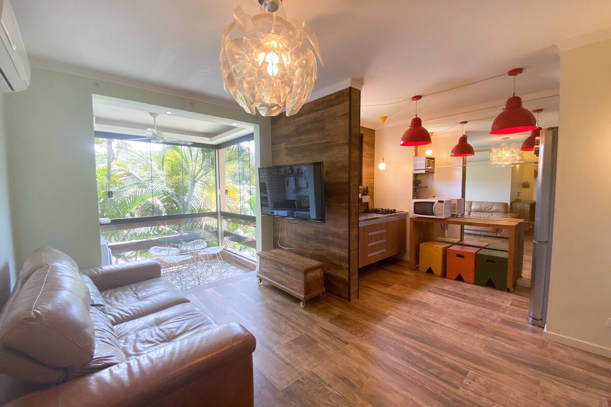 A modern living room with a leather sofa, a wooden dining area, and a kitchen with red pendant lights.