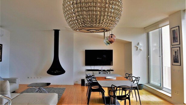 Un salon moderne comprenant un coin repas, un grand téléviseur et un lustre sphérique original.