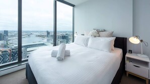 A modern hotel room with a large bed, white bedding, and a nightstand with a lamp. - Homely 1BR Apt Near Southern Cross Station w/ Pool (Melbourne)