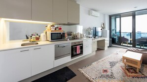 A modern kitchen with white cabinets, stainless steel appliances, and a large window overlooking a cityscape. - Homely 1BR Apt Near Southern Cross Station w/ Pool (Melbourne)