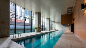 An indoor swimming pool with clear glass walls, a tiled floor, and a no diving sign. - Homely 1BR Apt Near Southern Cross Station w/ Pool (Melbourne)