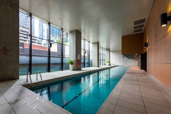 An indoor swimming pool with clear glass walls, a tiled floor, and a no diving sign.