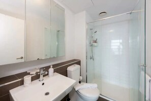 A modern bathroom with a glass-enclosed shower, a white sink, and a toilet.