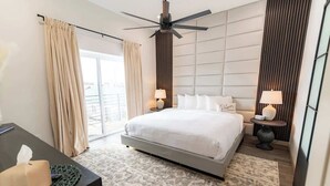 Une chambre d’hôtel moderne, dotée d’un grand lit, de deux lampes de chevet, d’un ventilateur de plafond et offrant une vue sur l’extérieur.