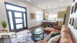 Un salon moderne avec un canapé en cuir marron, une table basse ronde et un coin repas, la cuisine étant visible au fond.
