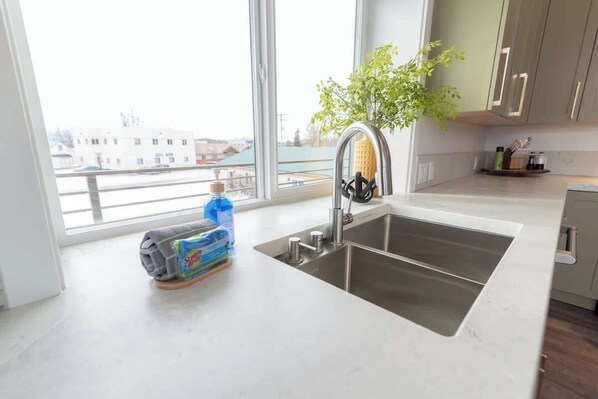 Une cuisine avec une grande fenêtre, un évier et une plante posée sur le plan de travail.