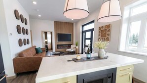 Une cuisine moderne dotée d’un îlot central, d’un four encastré et d’un four à micro-ondes. On y trouve également un coin repas avec une table et des chaises, ainsi qu’un salon avec un canapé et un téléviseur.