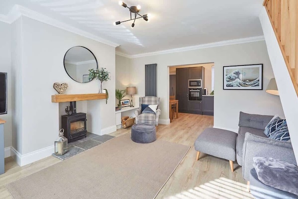 A living room with a fireplace, a sofa, a rug, and a kitchen in the background.