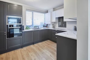 A modern kitchen with dark cabinetry, a built-in oven, and a window with blinds.
