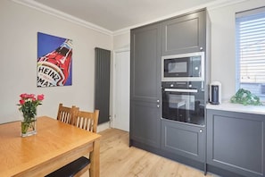 A modern kitchen with grey cabinets, a built-in microwave, and an oven. There is a dining table with chairs and a vase of flowers.