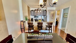 A modern kitchen with a central island, bar stools, and a dining table with potted plants. - Asian Themed, Beach-Front, Penthouse Condo, Huge Balcony, Free Beach Chairs! (Panama City Beach)