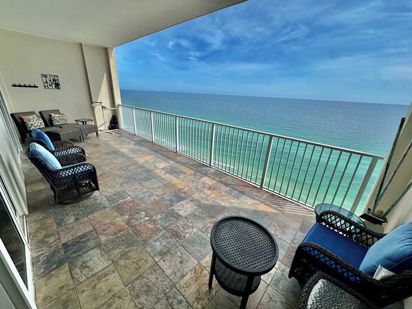 A balcony with wicker furniture, a round table, and a view of the ocean.