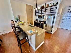 Uma cozinha com ilha central, micro-ondas, geladeira e pia.