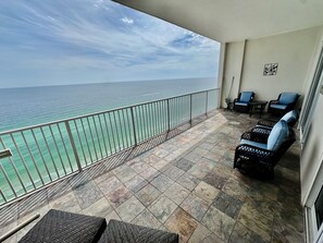 A balcony with a view of the ocean, wicker furniture, and a tiled floor.