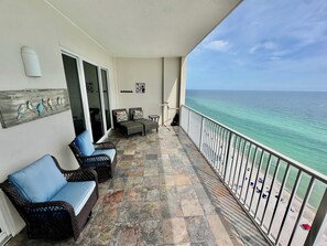 A balcony with wicker furniture, a bird art piece, and a view of the ocean.