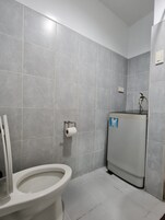 A bathroom with grey tiles, a toilet, a paper towel dispenser, and a water heater.