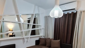 A modern living room with a sectional sofa, a glass coffee table, and a unique hanging light fixture. - Sea Residences - Condo R Us (Pasay)