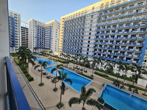 A high-rise hotel with multiple balconies, a swimming pool area with lounge chairs, and palm trees.