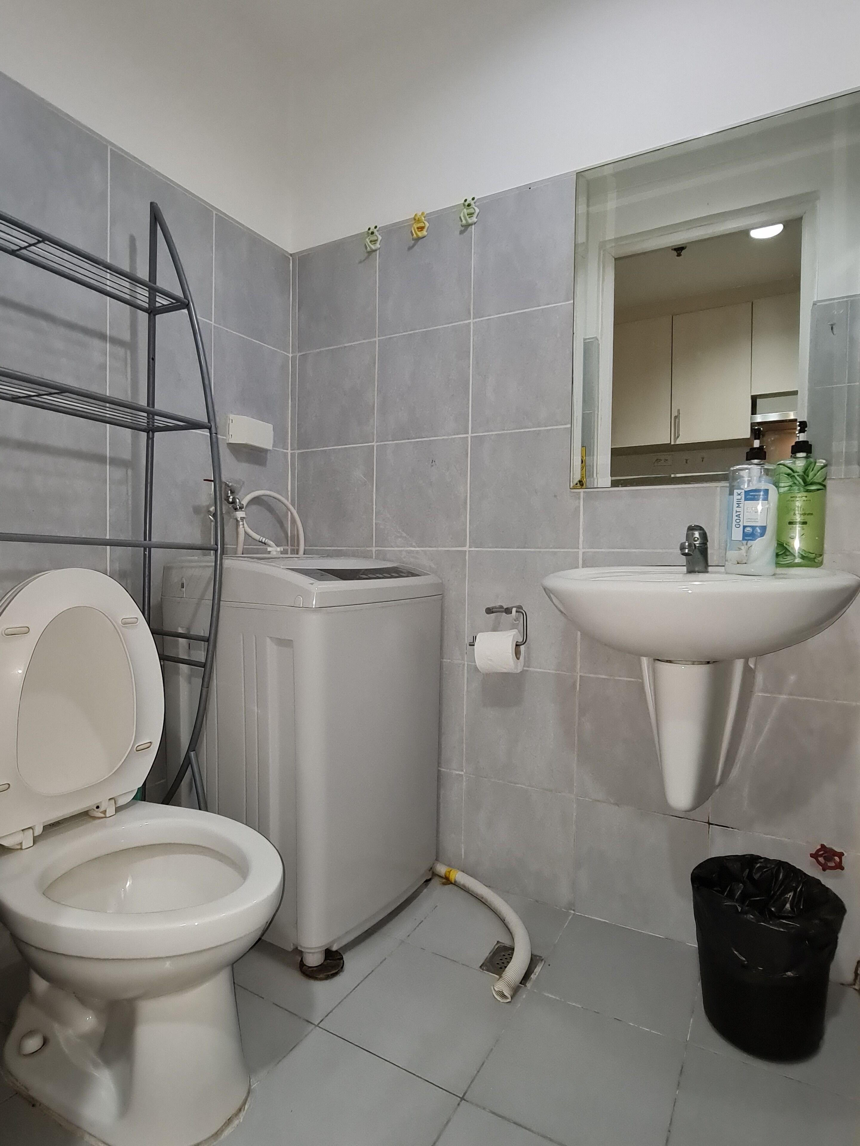 Et badeværelse med toilet, vaskemaskine, håndvask og en sort skraldespand.